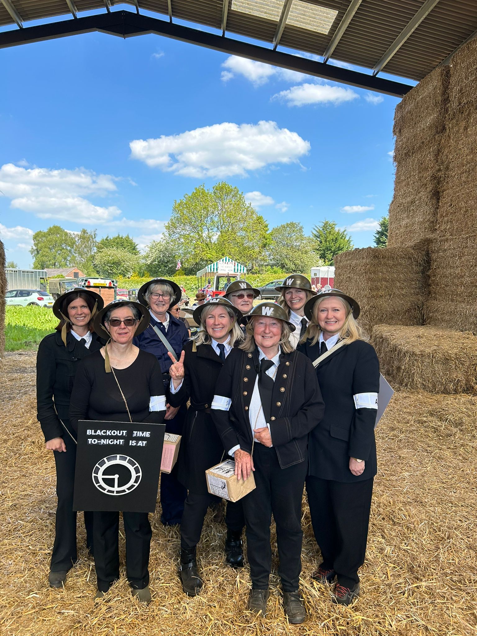 Choir members dressed in wartime warden costumes at an outdoor community event.