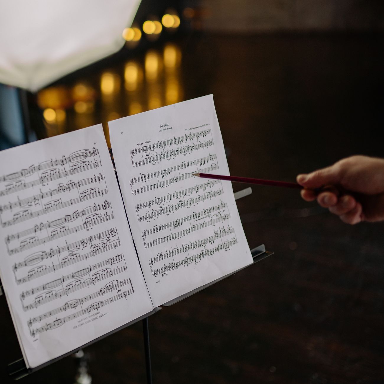 An instructor pointing at sheet music on a stand, guiding a rehearsal.