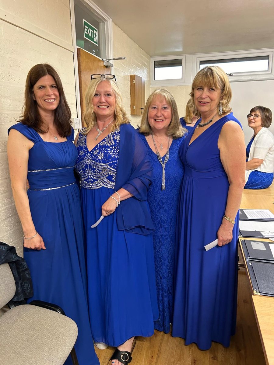 One Achord members in blue dresses, smiling together backstage before a performance.